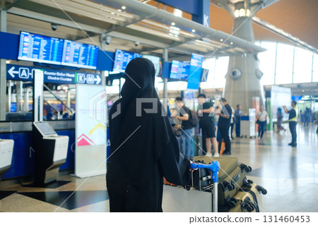 Woman in black abaya stands with luggage at airport check-in area during busy travel hours Woman in black abaya stands with luggage at airport check-in area during busy travel hours 131460453