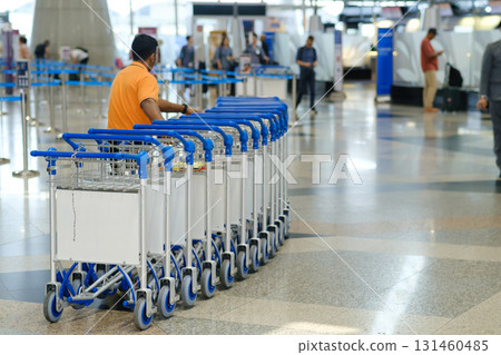 Busy day at the airport with a luggage trolley attendant organizing carts in a large terminal area Busy day at the airport with a luggage trolley attendant organizing carts in a large terminal area 131460485