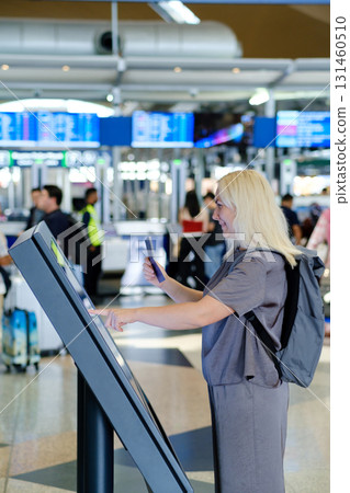 Traveler uses self-check-in kiosk at busy airport while preparing for upcoming flight to an international destination 131460510