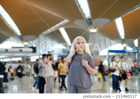Woman standing in a busy international airport terminal with people walking around and modern architecture in the background during daytime travel hours Woman standing in a busy international airport terminal with people walking around and modern architecture in the background during daytime travel hours 131460517