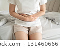 Young female suffering form stomach ache while sitting on a bed at home. Causes of abdominal pain include menstruation pain, gastritis, stomach ulcer, food poisoning, diarrhea or IBS. 131460666