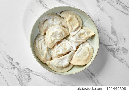 Delicious polish dumplings, pierogi, sprinkled with powdered sugar, resting in a bowl on marble surface Delicious polish dumplings, pierogi, sprinkled with powdered sugar, resting in a bowl on marble surface 131460808
