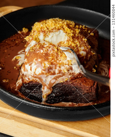 Fork digging into warm chocolate brownie with vanilla ice cream and cookie crumbles Fork digging into warm chocolate brownie with vanilla ice cream and cookie crumbles 131460844