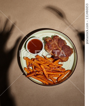 Grilled steak with sweet potato fries and barbecue sauce casting shadows on table 131460853