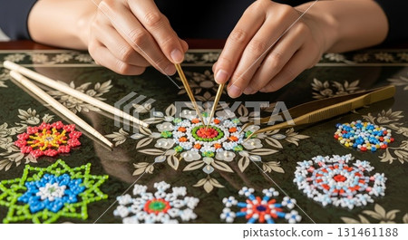 Asian woman hands using golden tweezers creating colorful beaded mandala flower pattern on dark wooden surface with multiple finished beadwork designs 131461188