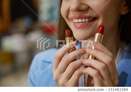 A woman is holding two different lipsticks right in front of her face A woman is holding two different lipsticks right in front of her face 131461369