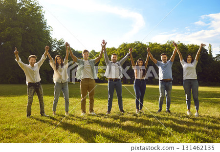 Group of happy excited friends standing in green summer park and holding up hands Group of happy excited friends standing in green summer park and holding up hands 131462135