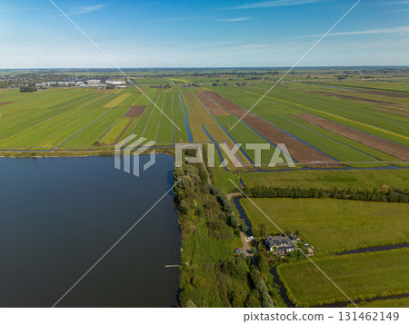 Aerial view of a rural landscape with a central road, water body, irrigated fields, and scattered houses. The scene highlights agricultural planning and natural integration. Aerial view of a rural landscape with a central road, water body, irrigated fields, and scattered houses. The scene highlights agricultural planning and natural integration. 131462149