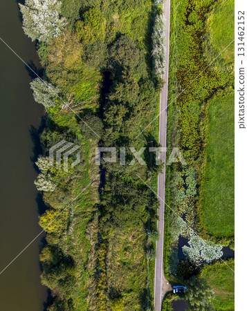 Aerial view of river bordered by forest and farmland, with a vertical road dividing lush vegetation and rectangular fields highlighting land use and ecological contrast. 131462152