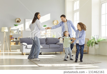 Funny active dancing family of young adult parents and cute small children together in living room  131462161