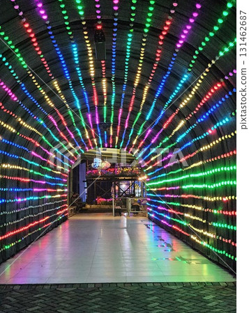 A stunning tunnel is illuminated by thousands of colorful LED lights, creating a mesmerizing and vibrant archway that leads into a distant, brightly lit building. 131462687