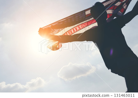 Celebrating American Freedom. Patriotic Man Holding Flag Against the Sun Celebrating American Freedom. Patriotic Man Holding Flag Against the Sun 131463011