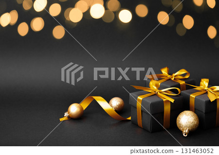Black gift box with golden ribbon bow on black background 131463052