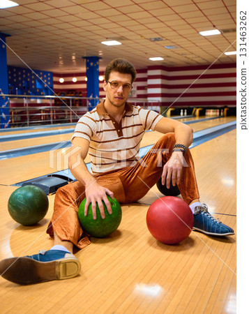 Man in striped polo and vintage trousers posing on bowling lane with colorful balls Man in striped polo and vintage trousers posing on bowling lane with colorful balls 131463262
