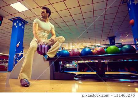Stylish man sitting on bench with bowling balls in colorful retro atmosphere Stylish man sitting on bench with bowling balls in colorful retro atmosphere 131463270