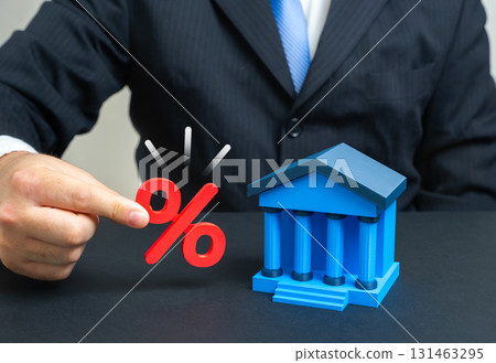 A businessman holds interest near a bank building. Inflation and deposits. Concept of capital growth, monetary risks, savings, loans, economic policy, investments and financial stability. A businessman holds interest near a bank building. Inflation and deposits. Concept of capital growth, monetary risks, savings, loans, economic policy, investments and financial stability. 131463295
