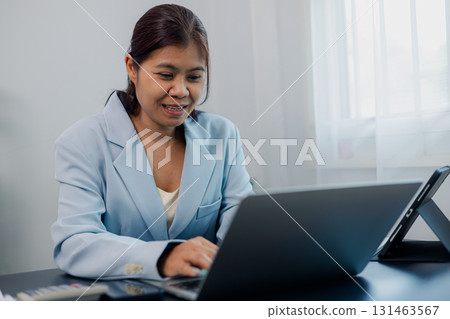 Asian businesswoman smiling while working on laptop during online meeting at office 131463567