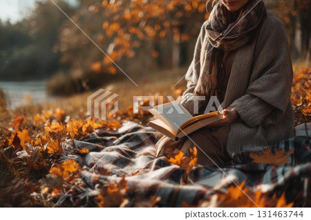 Woman reading book on blanket in park under autumn leaves enjoying peaceful moment 131463744