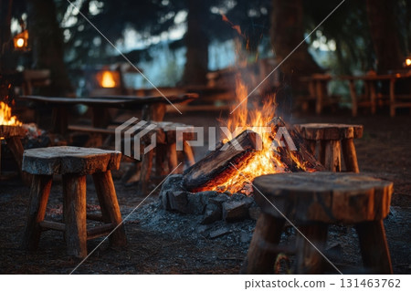 Cozy campfire with wooden stools in pine forest, warm embers glowing in early evening light 131463762