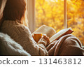 Woman in cozy sweater by window with book 131463812