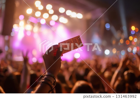 Hand holding concert ticket above crowd, colorful lights, live music excitement, spontaneous trip feeling 131463992