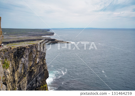 Dramatic cliffs meet the vast Atlantic Ocean in Ireland, with a clear sky overhead. 131464259
