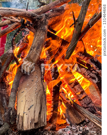 Blazing campfire with vibrant orange and yellow flames consuming wooden logs, radiating comforting warmth for exhilarating outdoor adventure and camping 131464668