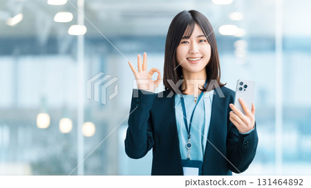 A smiling woman/businesswoman holding a smartphone and making an OK pose 131464892