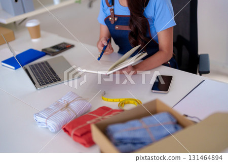 Asian adult woman entrepreneur managing online clothing business preparing orders customers working home office digital retail small business ecommerce startup 131464894