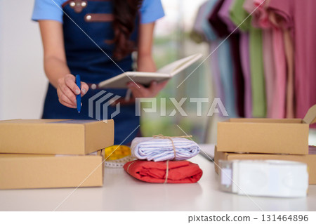 Adult Asian woman entrepreneur manages online clothing store orders packing delivery logistics diligently preparing shipments in home office workspace for ecommerce success 131464896