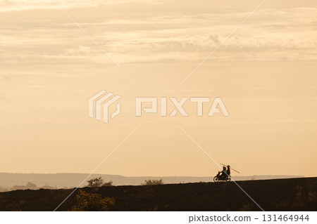 Silhouette of two men biker and a motorcycle on the road with sunset light background Silhouette of two men biker and a motorcycle on the road with sunset light background 131464944