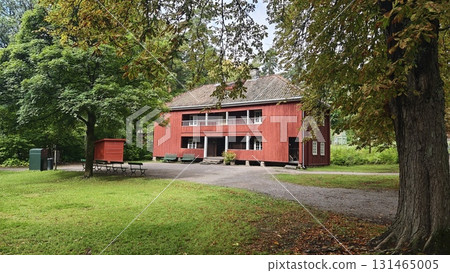 Traditional red wooden house surrounded by lush greenery and trees in a peaceful park setting. 131465005