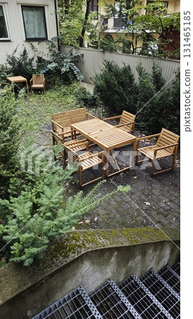 Outdoor backyard garden with wooden furniture set on stone pavement surrounded by green bushes. Outdoor backyard garden with wooden furniture set on stone pavement surrounded by green bushes. 131465185