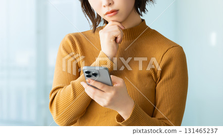 Woman/businesswoman thinking while looking at smartphone Woman/businesswoman thinking while looking at smartphone 131465237