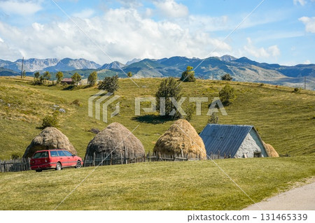 Scenic view of rolling hills in the mountains with a traditional clay house, haystacks, and a red car nearby, highlighting rustic rural landscape ideal for travel, lifestyle, and nature projects. 131465339