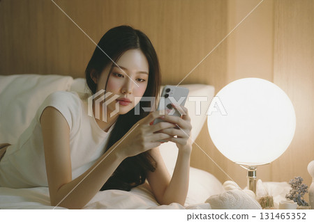 Woman is laying on a bed and looking at her cell phone 131465352
