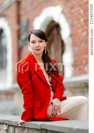Elegant businesswoman wearing red jacket sitting on a low wall Elegant businesswoman wearing red jacket sitting on a low wall 131465509
