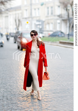 Stylish businesswoman walking down cobblestone street in red coat Stylish businesswoman walking down cobblestone street in red coat 131465510