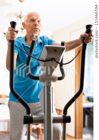 Old man using elliptic trainer at home 131466394