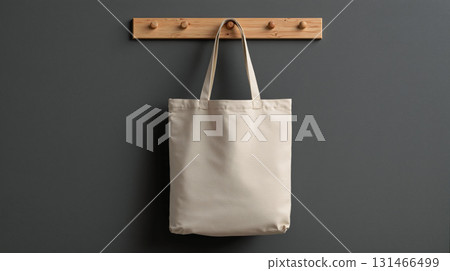 Simple tote bag hanging on a wooden hook against a gray wall showcasing a minimalist design 131466499