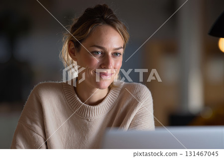 Freelancer smiling while engaging in a video call from a cozy workspace at home during evening hours 131467045