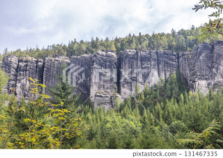 Adrspach-Teplice Rocks, sandstone formations in Hradec Kralove Region in the Czech Republic, Europe. Jagged rock formations reach skyward, standing guard over a lush green forest under a cloudy sky. Adrspach-Teplice Rocks, sandstone formations in Hradec Kralove Region in the Czech Republic, Europe. Jagged rock formations reach skyward, standing guard over a lush green forest under a cloudy sky. 131467335