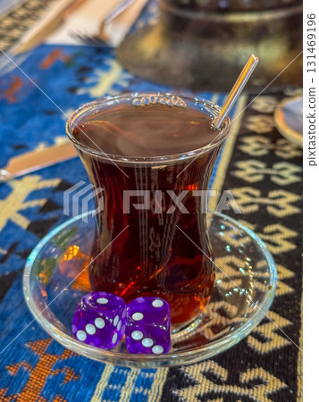 Turkish tea glass with purple dice on a patterned table for casual game night Turkish tea glass with purple dice on a patterned table for casual game night 131469196