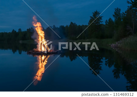 A bonfire burning brightly on a raft in the middle of a dark blue lake 131469312