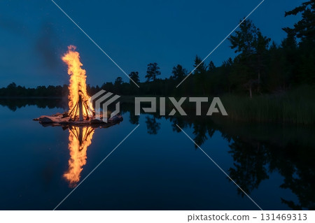 Bonfire burning on a raft in the middle of a lake at night with reflection 131469313