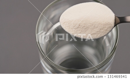 Close-up of a spoon with collagen or protein powder held over a glass of water. Concept of dietary supplement, healthy lifestyle, nutrition, beauty care and soluble wellness product preparation Close-up of a spoon with collagen or protein powder held over a glass of water. Concept of dietary supplement, healthy lifestyle, nutrition, beauty care and soluble wellness product preparation 131469341