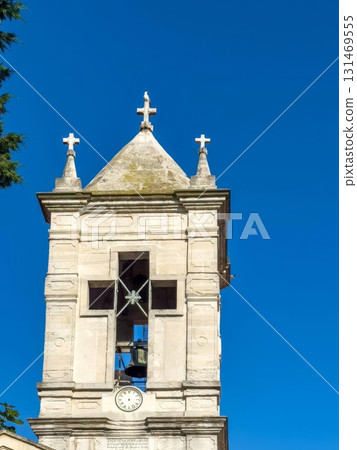 An old bell tower with a clock against the background of a bright blue sky. 131469555