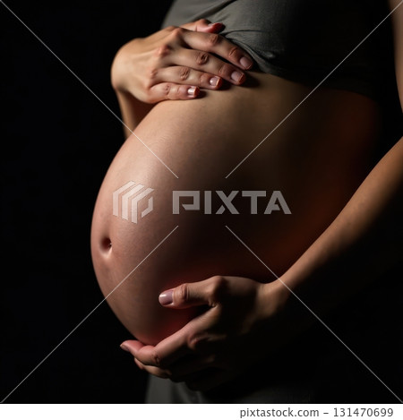 Pregnant woman holding her belly on black background 131470699