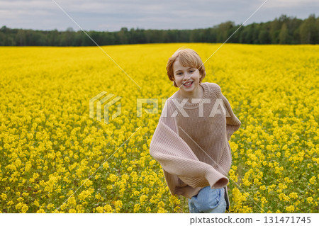 Smiling girl in oversized beige sweater standing in yellow flower field under cloudy sky Smiling girl in oversized beige sweater standing in yellow flower field under cloudy sky 131471745