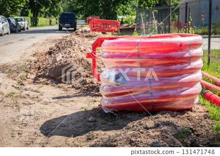 Red Corrugated Conduit Coils on Roadside at Construction Site for Underground Cable Installation 131471748